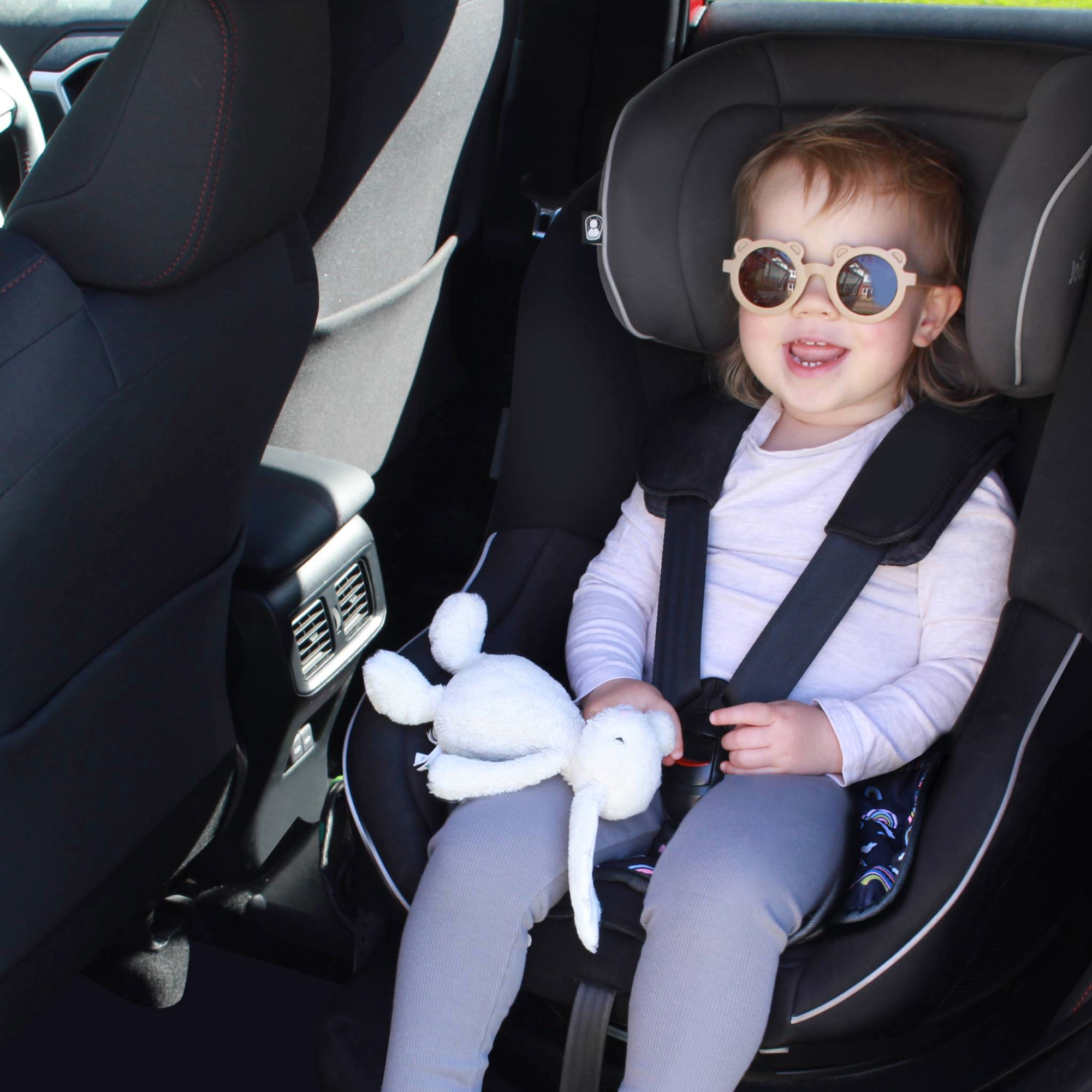 Child in a car seat using a Hygge rainbow print car seat protector
