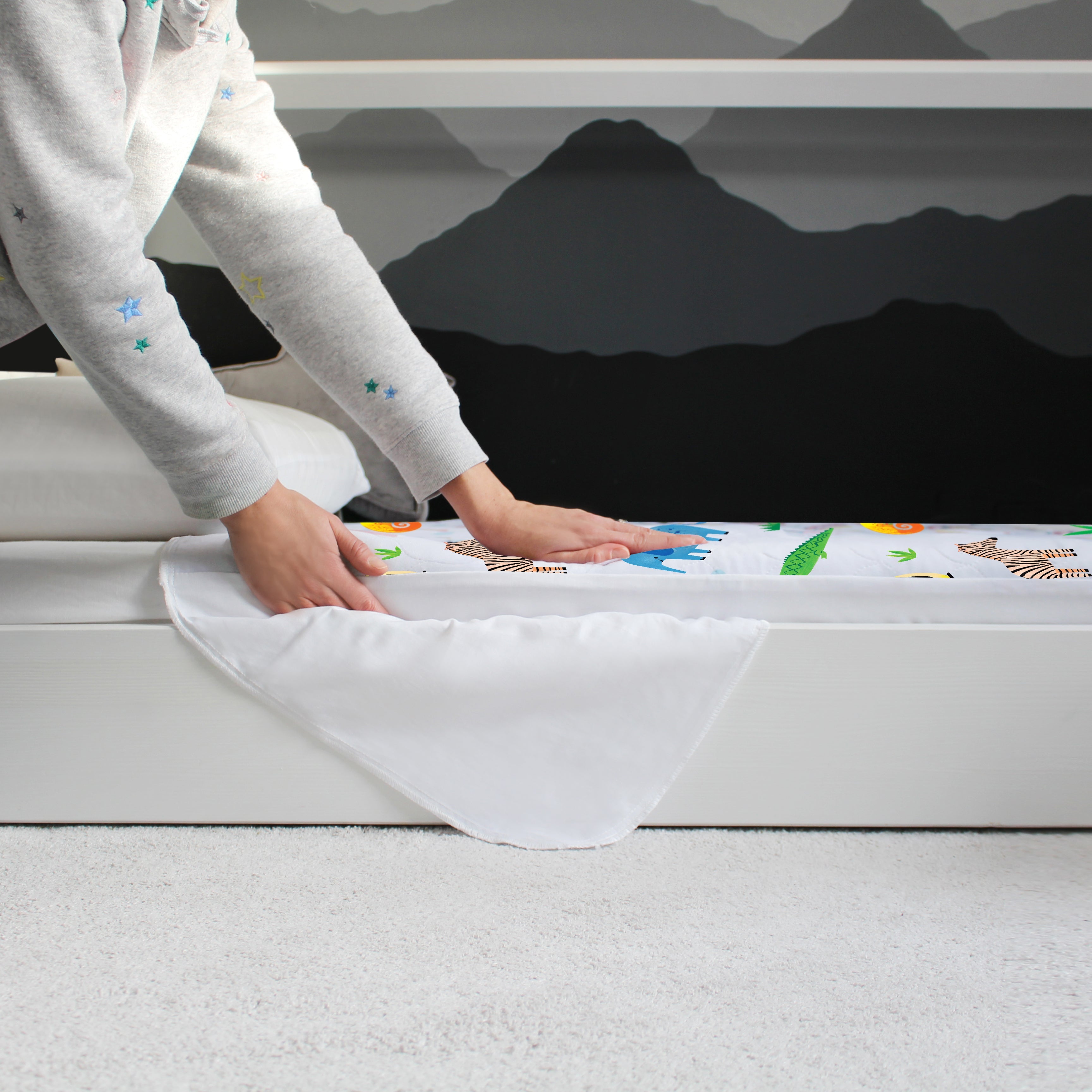 Person fitting a Safari print Hygge waterproof bed pad onto a child’s bed