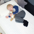 A young child asleep on a white bamboo waterproof mattress protector.