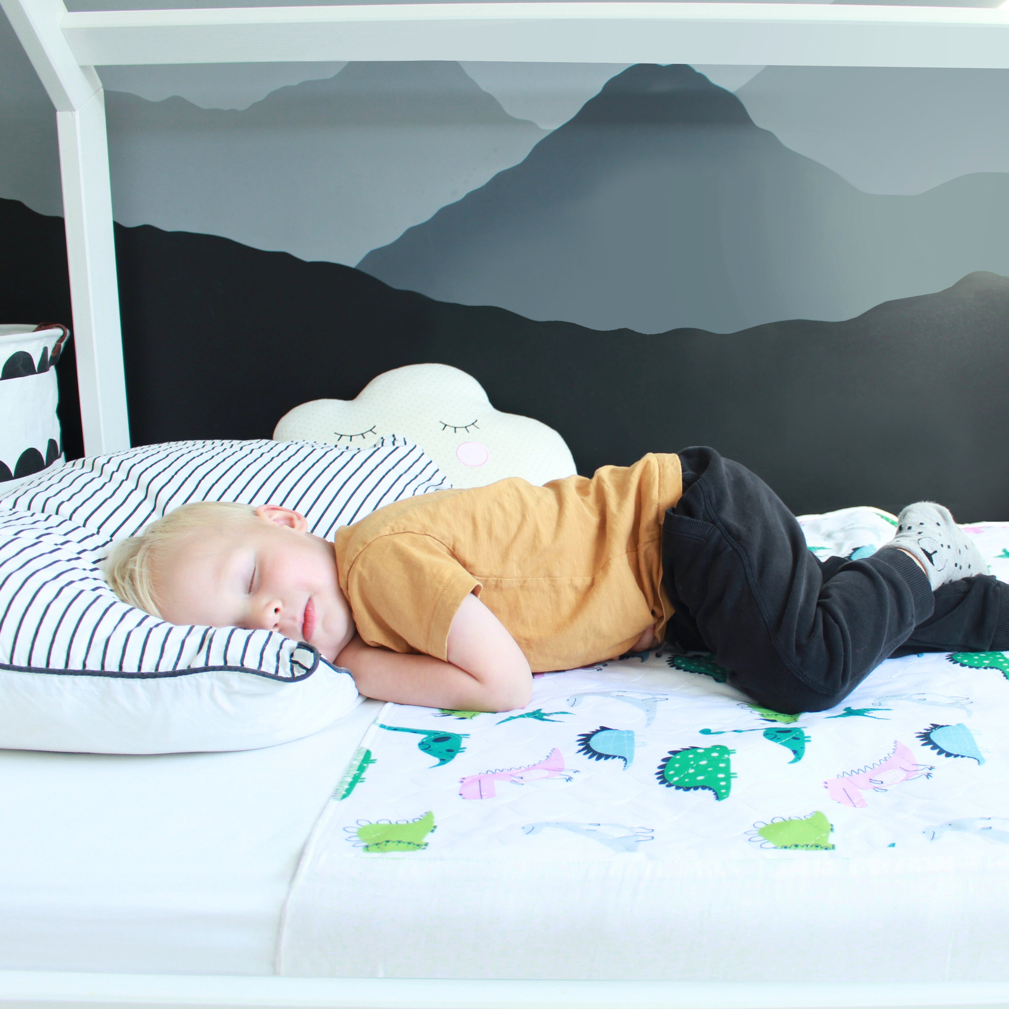 Child sleeping on a bed with a dinosaur-patterned waterproof mattress protector