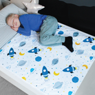 A child lying on a single bed with a white mattress protector featuring a space-themed design with rockets and planets.