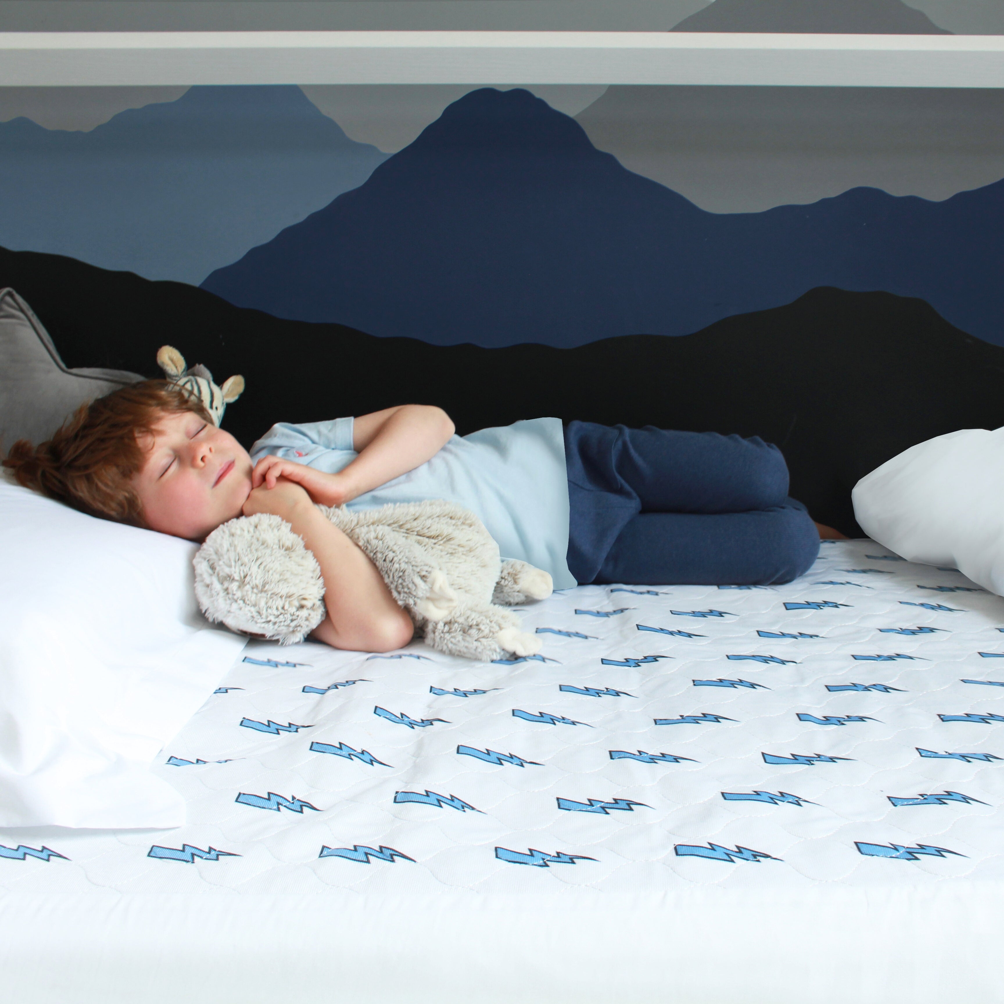 Boy cuddling his toys lying on the lightening bolt waterproof mattress protector.