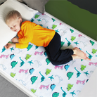 A child lying on a single bed with a waterproof dinosaur mattress protector.