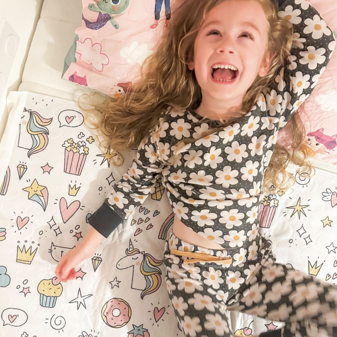 Child in floral pyjamas jumping on a bed with the unicorn design waterproof bed protector