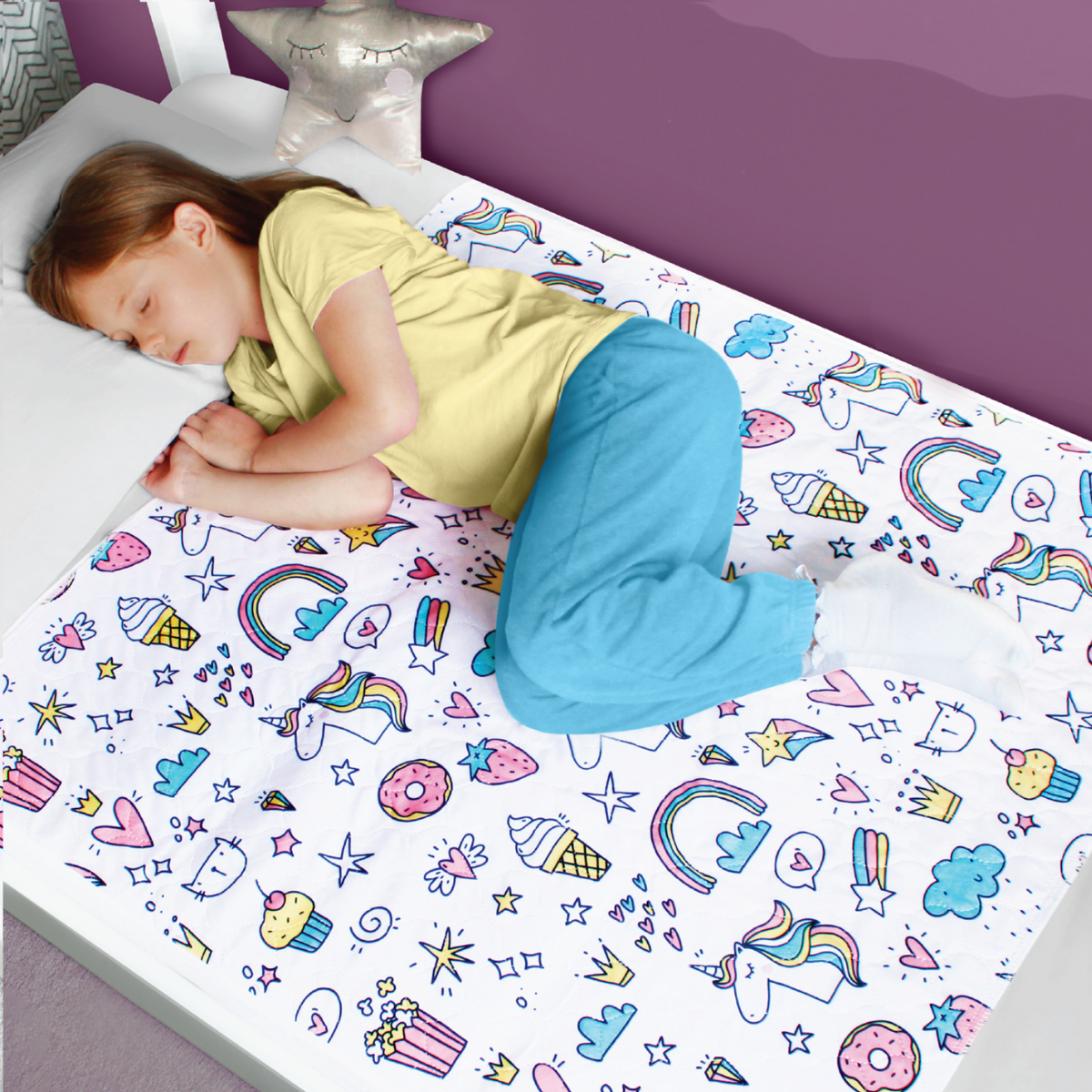 Child lying on a bed with the unicorn design waterproof bed sheet featuring unicorns, rainbows, and other cartoon elements.