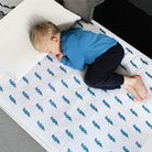 A child lying on a single mattress protector with a lightning bolt pattern. The protector is white with blue lightning bolts and is fitted on top of a bed with the child on top.