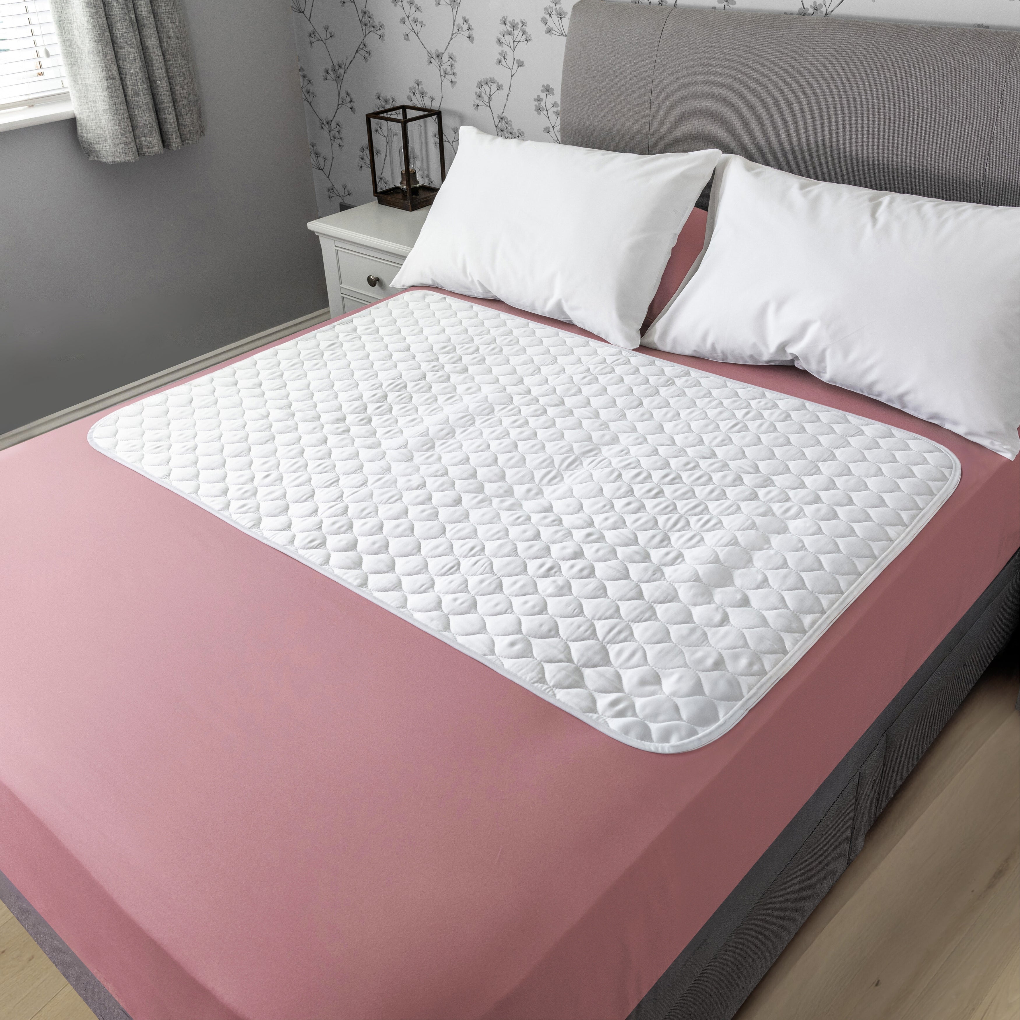 Organic bamboo 2-Way Fit Incontinence Pad on a bed with pink sheets in a bedroom setting.