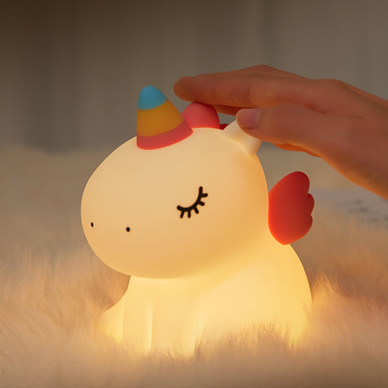 A night light turned on designed to look like a unicorn with a hand pressing on top.