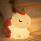 A night light turned on designed to look like a unicorn with a hand holding it at the back.
