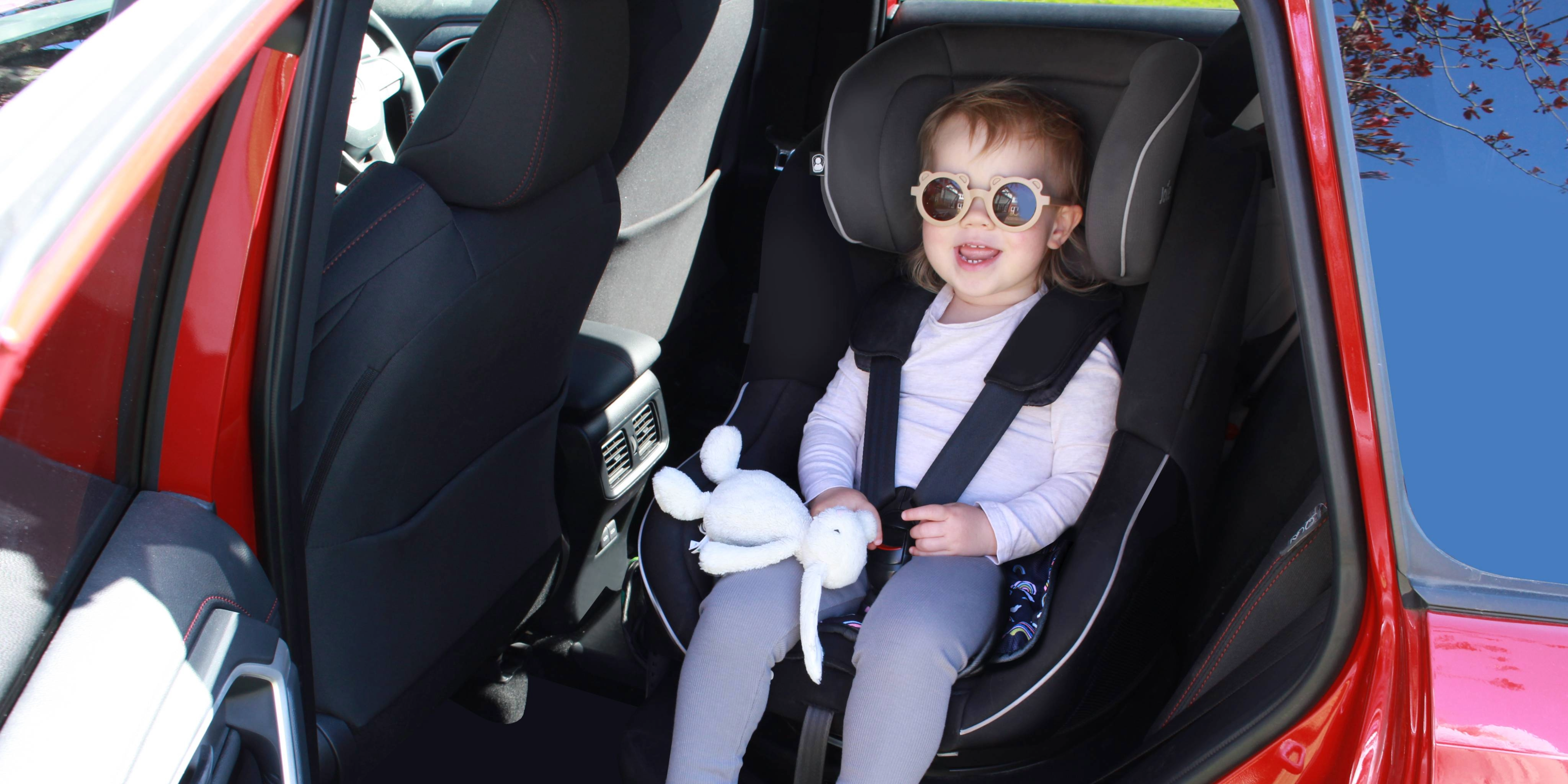 Child in a car seat using a Hygge rainbow print car seat protector
