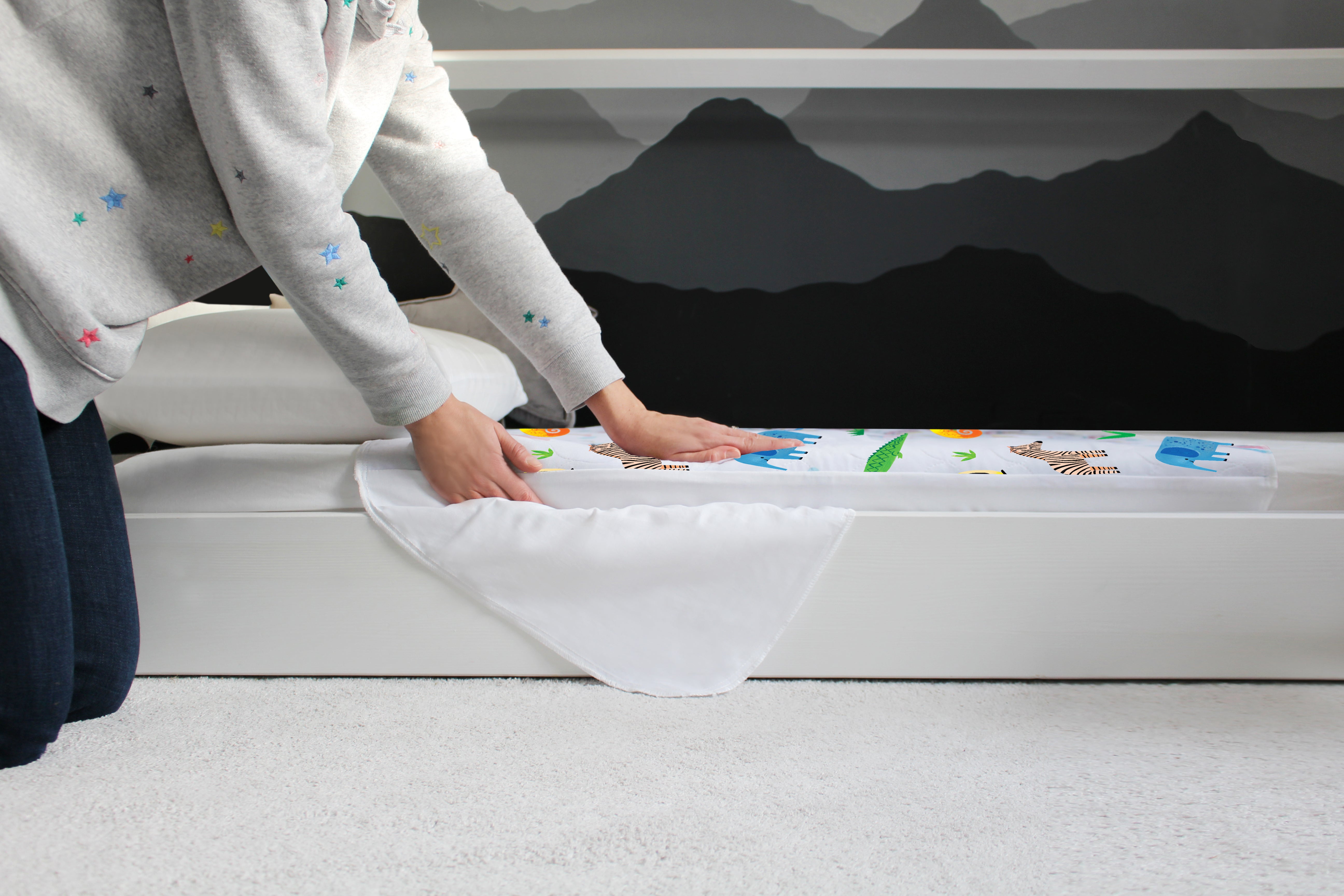 Person fitting a Safari print Hygge waterproof bed pad onto a child’s bed