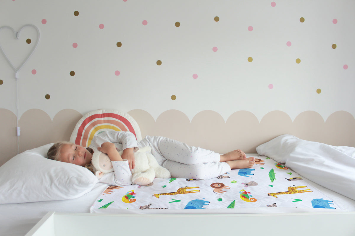 Child sleeping on a Safari print Hygge waterproof bed pad while cuddling a teddy bear