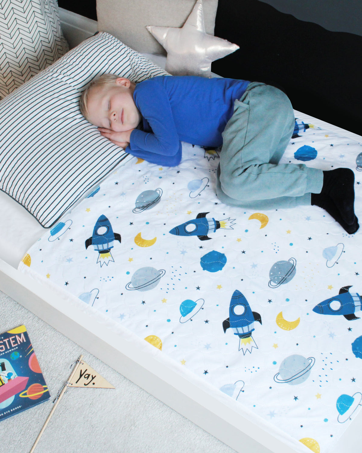 Child sleeping on a white bed with a Hygge waterproof bed pad featuring a space print