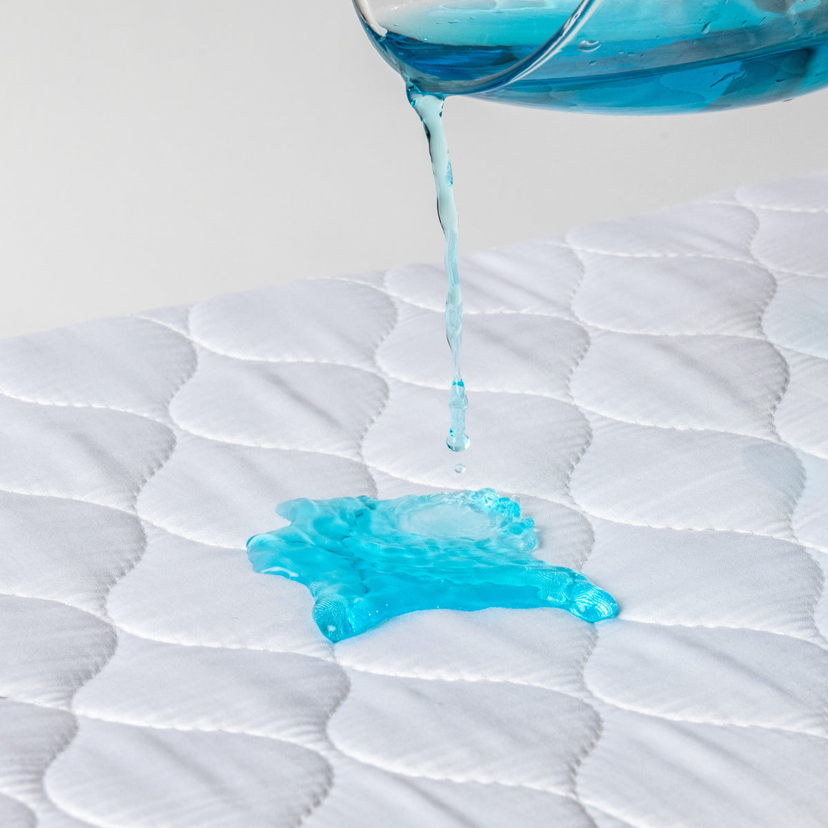 Liquid poured onto a white Hygge waterproof bed pad to demonstrate waterproof protection