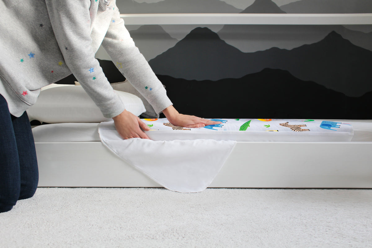 Person fitting a Safari print Hygge waterproof bed pad onto a child’s bed