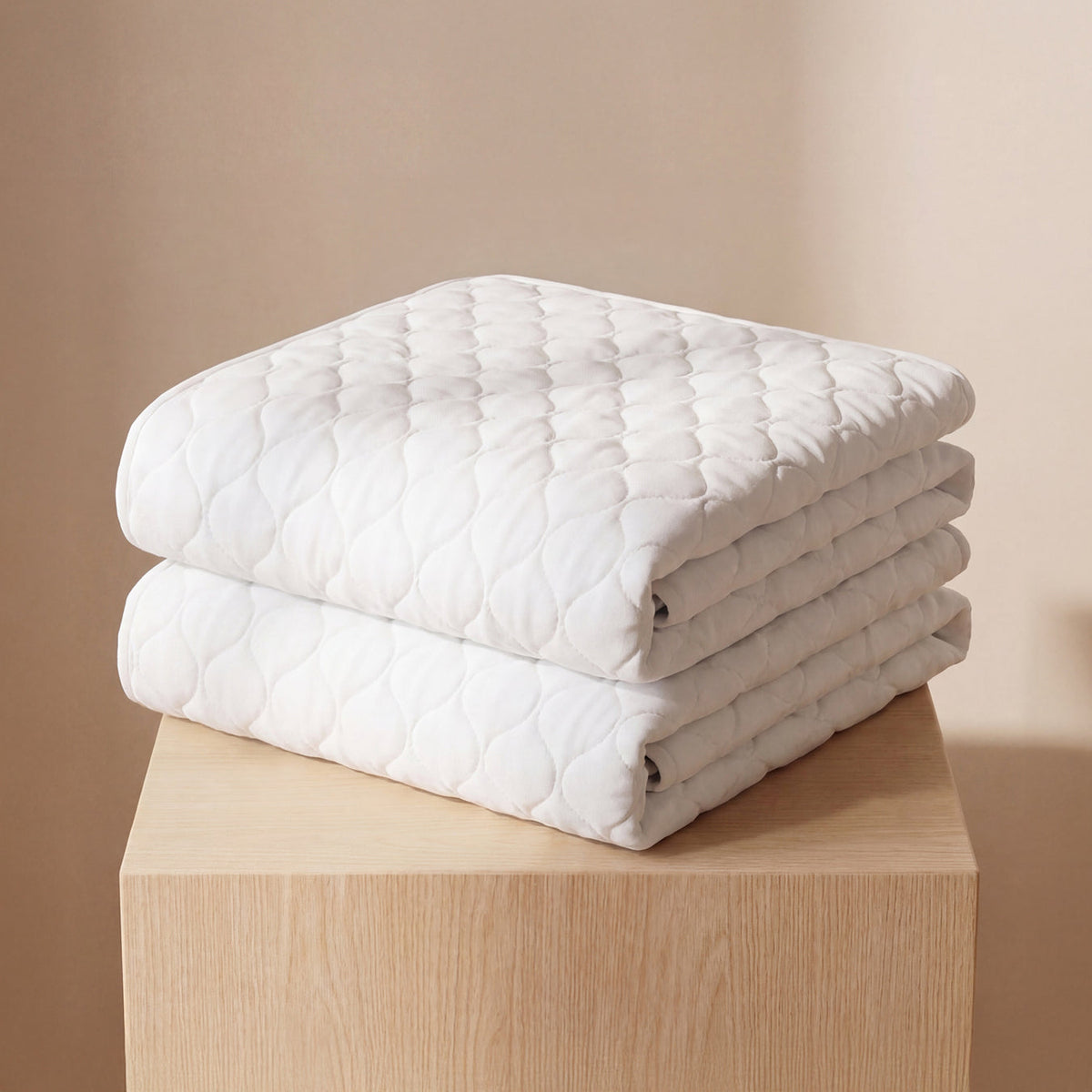 Folded white Hygge bamboo waterproof bed pads stacked on a wooden table